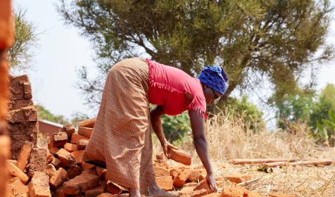 Aline Nibogora bending over to select good baked bricks from the brick kiln for her new house under construction on August 1st 2023 in Kayagoro village, Makamba, Burundi.