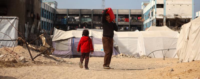 In Gaza, a man holds a bucket while a young girl walks next to him
